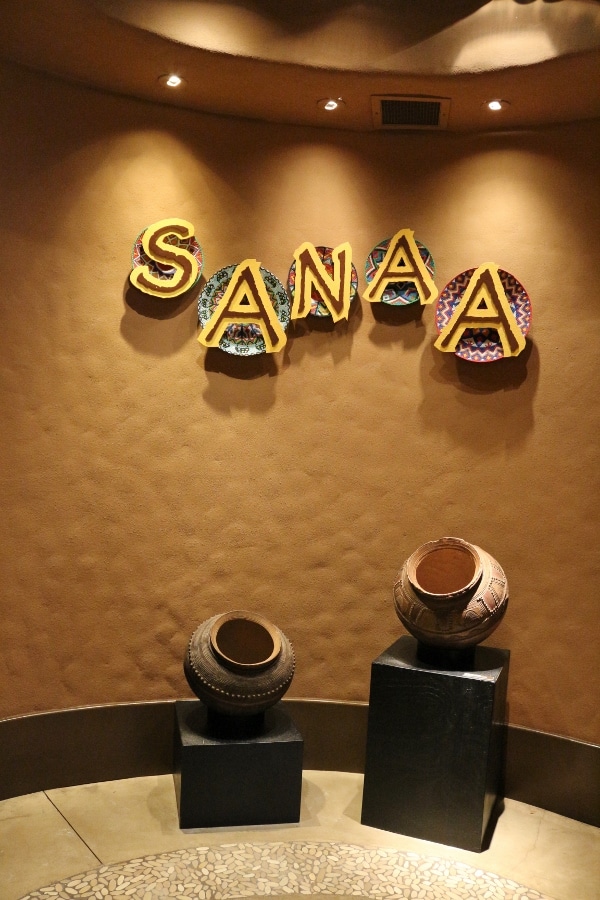 a sign that says Sanaa over a couple African artifacts on display