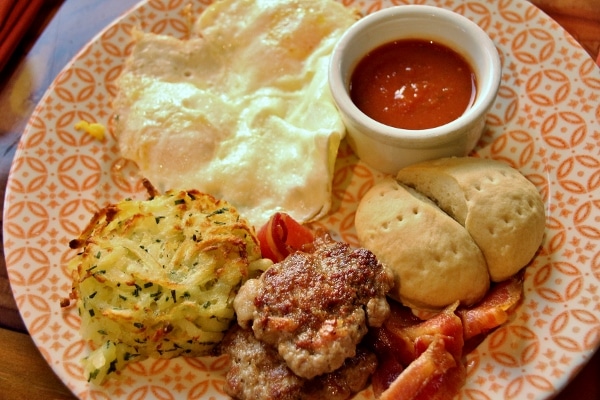 a breakfast platter with eggs, potato pancake, sausage patties, small biscuit, and sauce