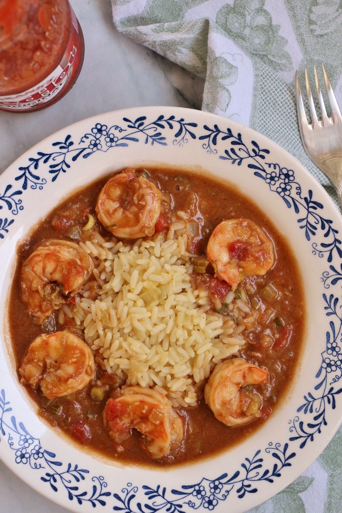 overhead view of a bowl of shrimp etouffee with rice and hot sauce beside it