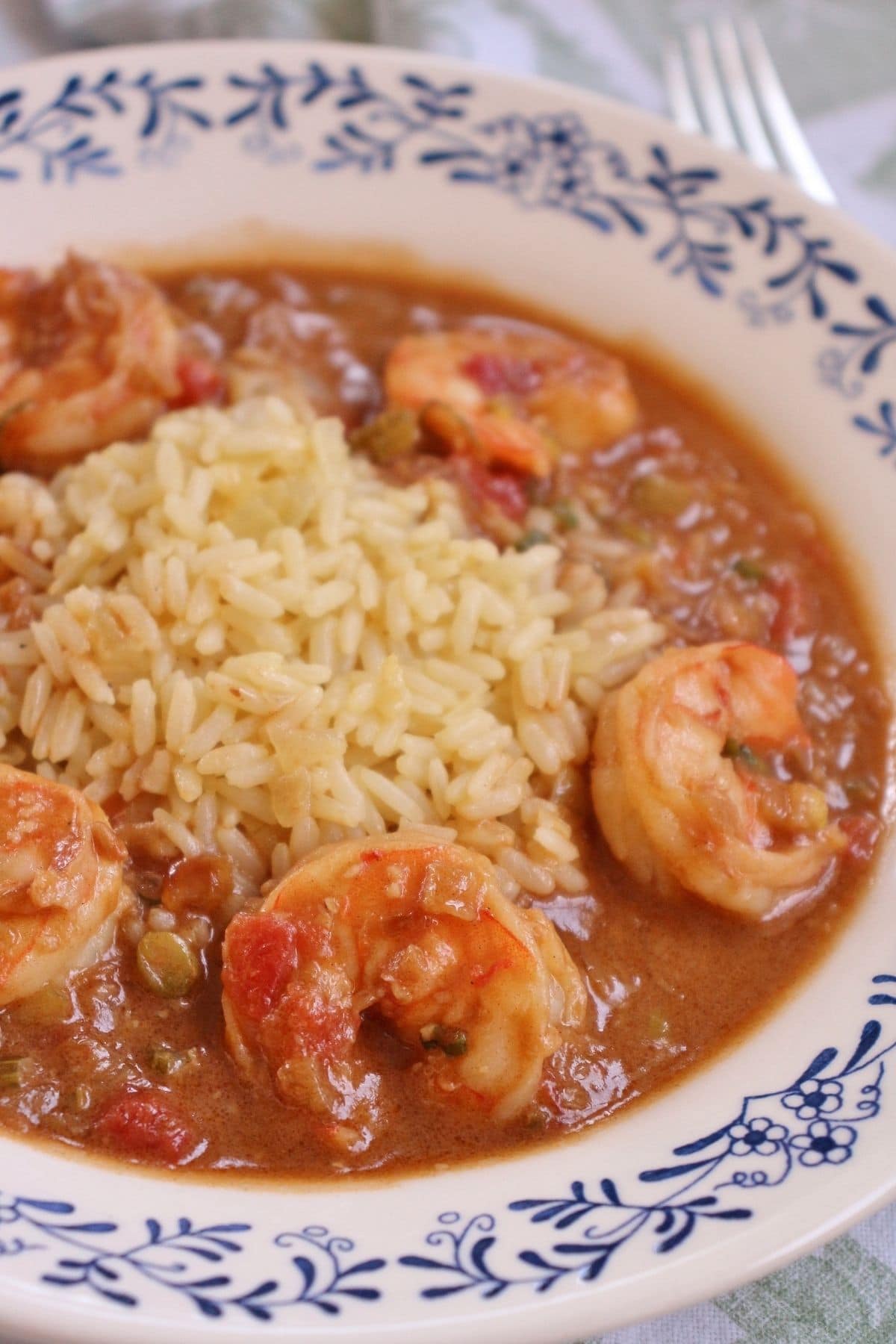 side closeup of a shallow white and blue bowl filled with rice and shrimp etouffee