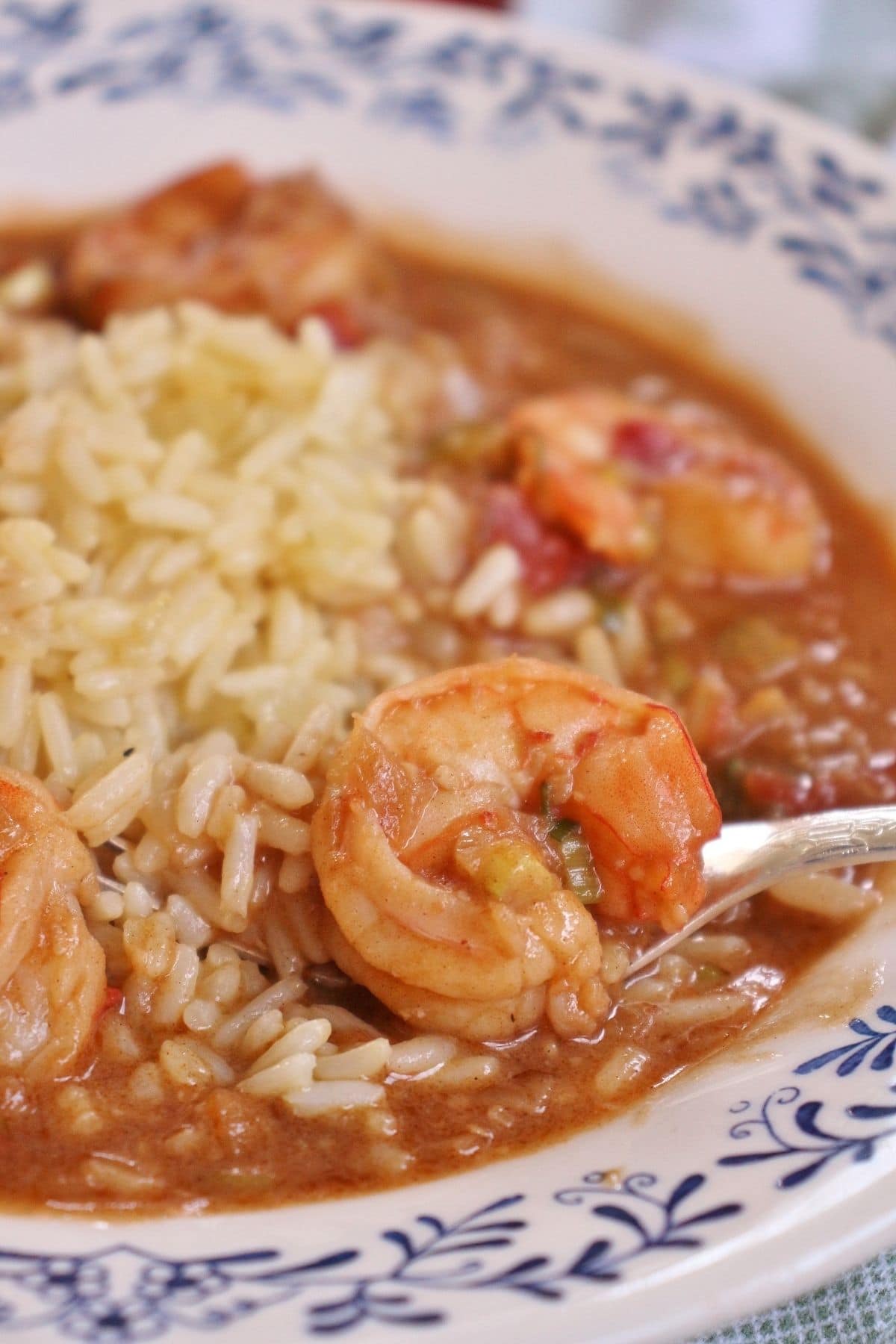 closeup of a shallow bowl of shrimp etouffee with rice and a fork scooping some up