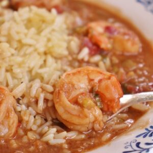 closeup of a shallow bowl of shrimp etouffee with rice and a fork scooping some up
