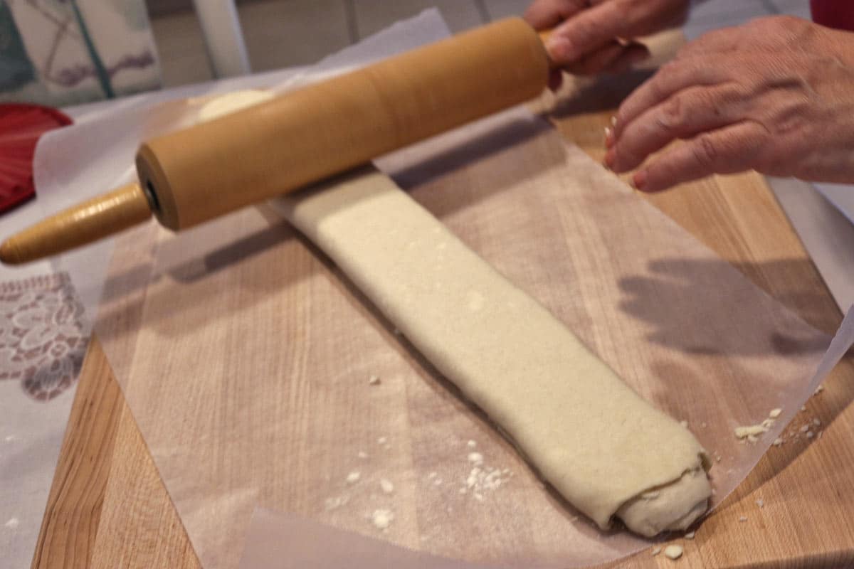 Flatting the gata roulade with a rolling pin on a wooden board.