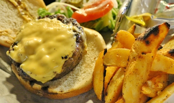 overhead view of a cheeseburger without the top bun, served with potato wedges