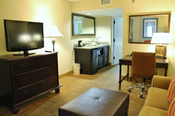 A living room area in a hotel room with a television and a desk