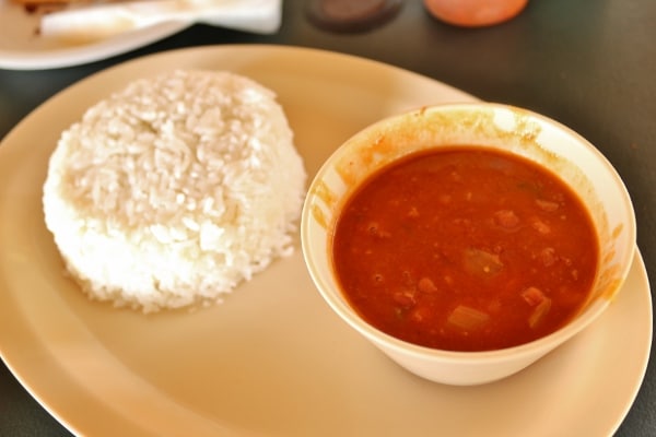 a pile of rice with a bowl of stewed beans next to it