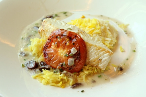 grilled fish served with a roasted tomato and rice on a white plate