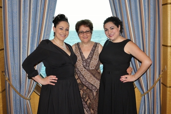 three women in formal dresses posing in front of a porthole on a cruise ship