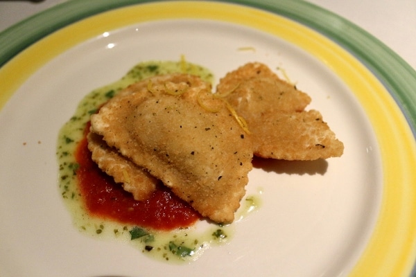 A plate of fried ravioli with tomato sauce and pesto