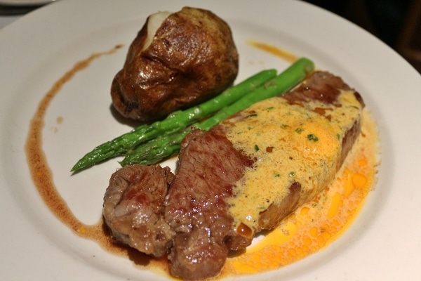 steak with a butter sauce, asparagus, and a baked potato on a plate