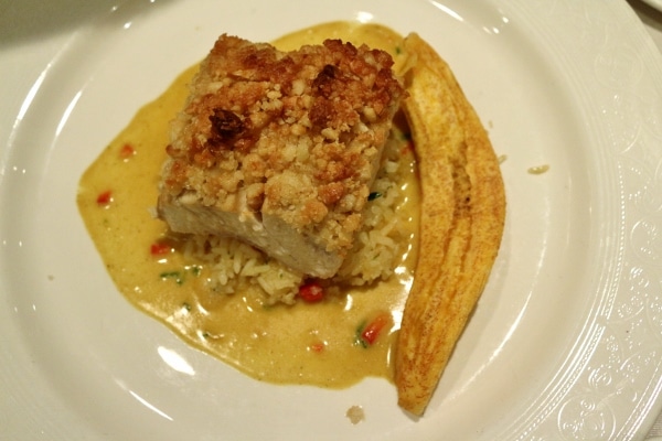 a macadamia nut crusted piece of fish served over rice with a plantain chip