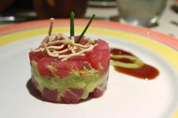 a raw tuna and avocado tower on a plate with sauce on the side