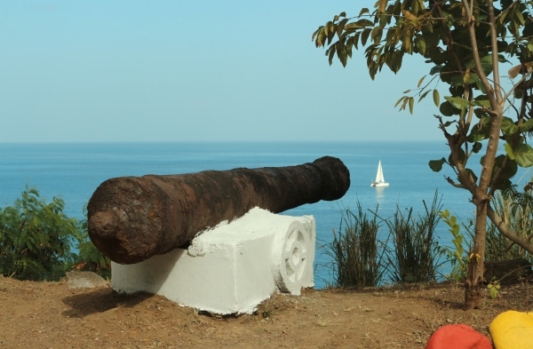 an old metal cannon pointing toward the sea in the direction of a sailboat