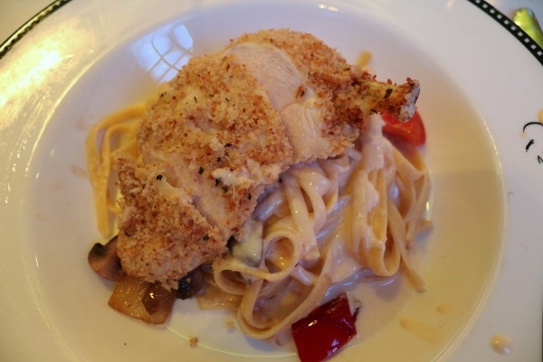 A plate of fettuccine in a creamy sauce topped with a breaded chicken breast