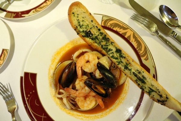 a seafood stew with a long piece of garlic bread on the side