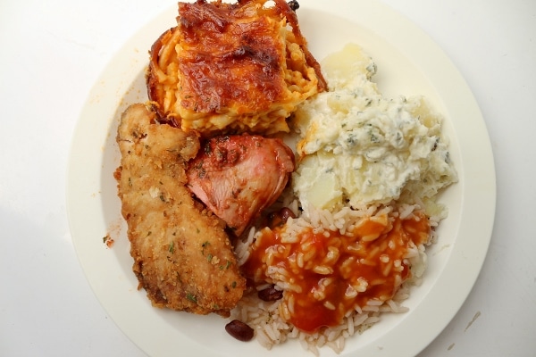 a plate of lasagna, fish, chicken, potato salad, and rice with tomato sauce