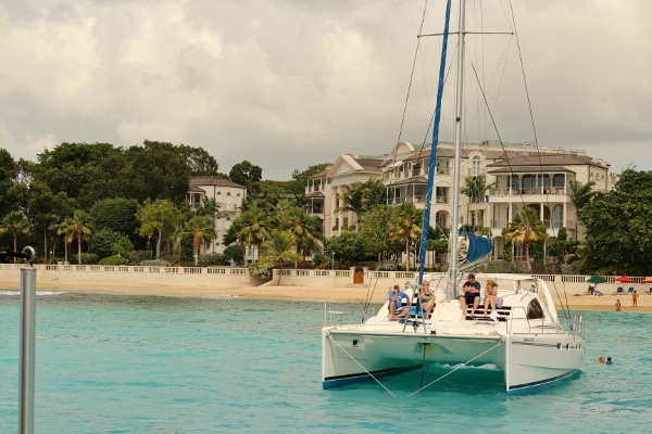 a catamaran in the water in front of a beach and beach-side mansions