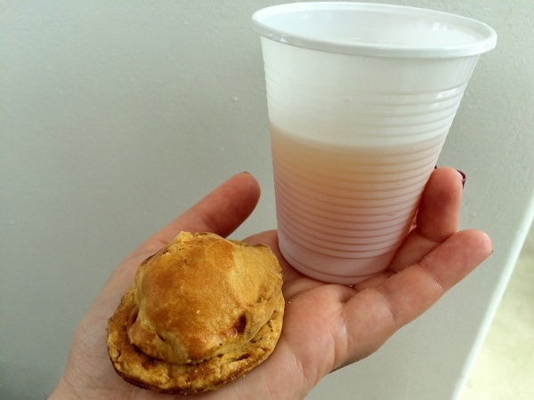 a hand holding a drink in a plastic cup and a small pastry