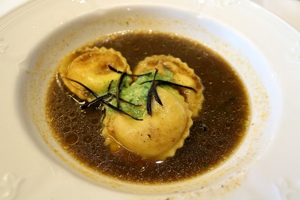 three lobster raviolis in a dark broth