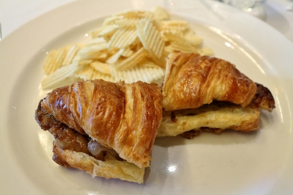 a croissant sandwich served with potato chips on a white plate