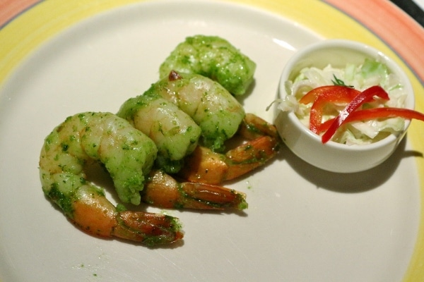 a row of shrimp in pesto sauce on a white plate
