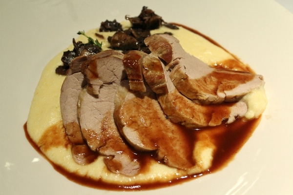 A plate sliced pork tenderloin served over polenta