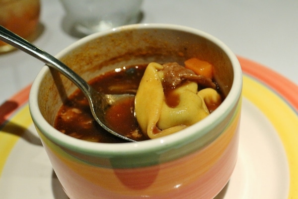 a spoon lifting a tortellini out of a cup of soup