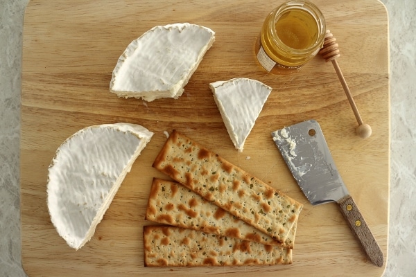 overhead view of a cheese board with Camembert cheese, crackers and honey