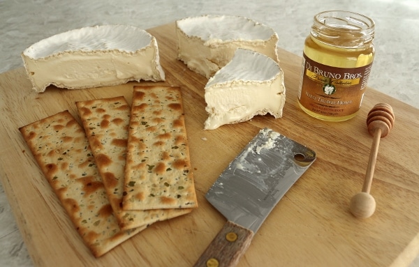 a wooden board topped with Camembert cheese, crackers, and white truffle honey