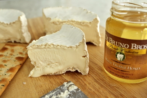 a closeup of Camembert cheese and white truffle honey on a wooden board