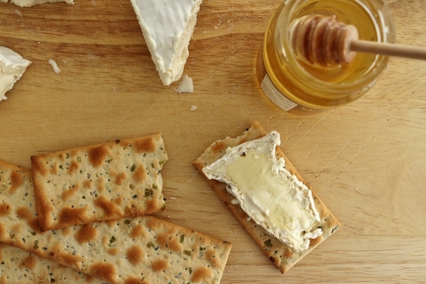 a slice of Camembert cheese on a cracker with honey over the top