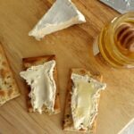 overhead view of two slices of Camembert cheese on crackers with honey