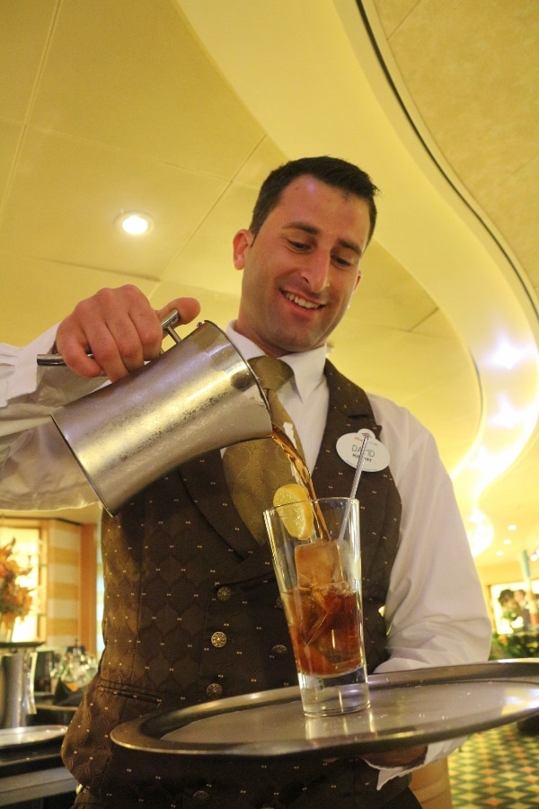 A man pouring a glass of iced tea from a metal pitcher