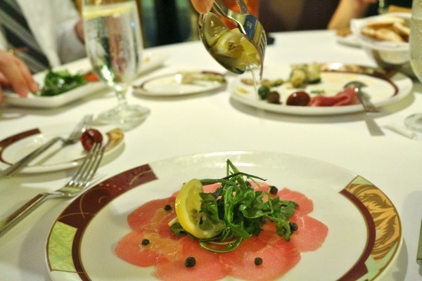 tuna carpaccio on a plate with greens and a lemon wedge