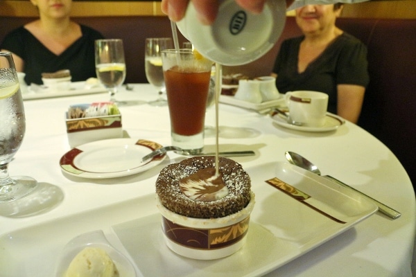 A person pouring sauces over a chocolate souffle
