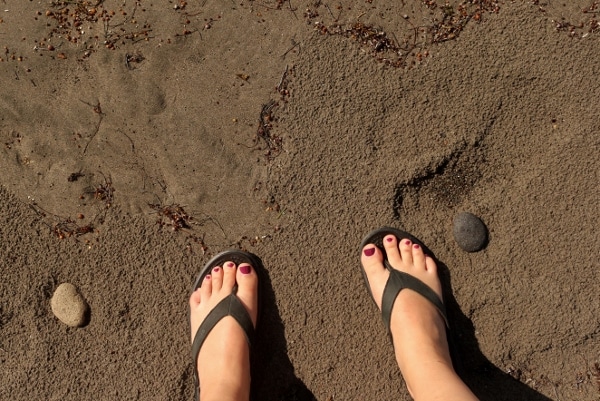 A person\'s feet standing on a black sand beach