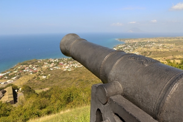 a metal cannon overlooking a city and sea below