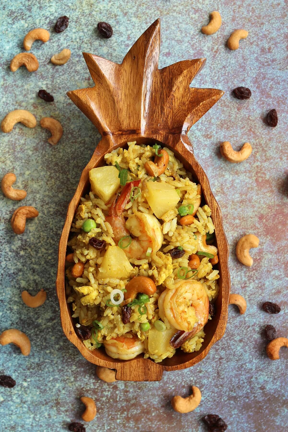 overhead view of fried rice in a pineapple bowl with cashews and raisins scattered around it