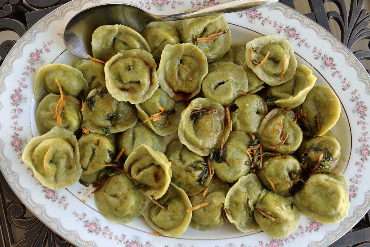 An oval white platter with decorative edges topped with green tortellini-shaped fish dumplings.