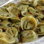 A platter of green tortellini-shaped fish dumplings topped with ginger soy sauce.