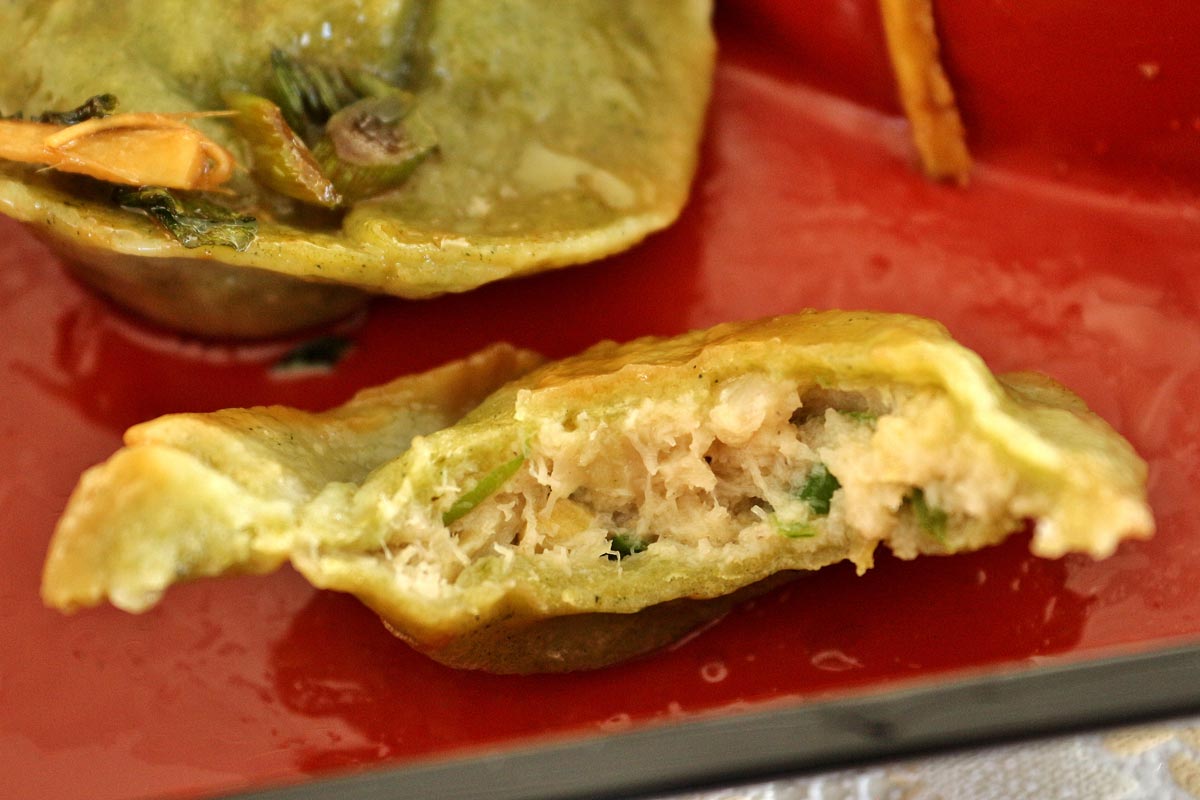 A half-eaten dumpling with green dough showing off the pale white fish filling inside.