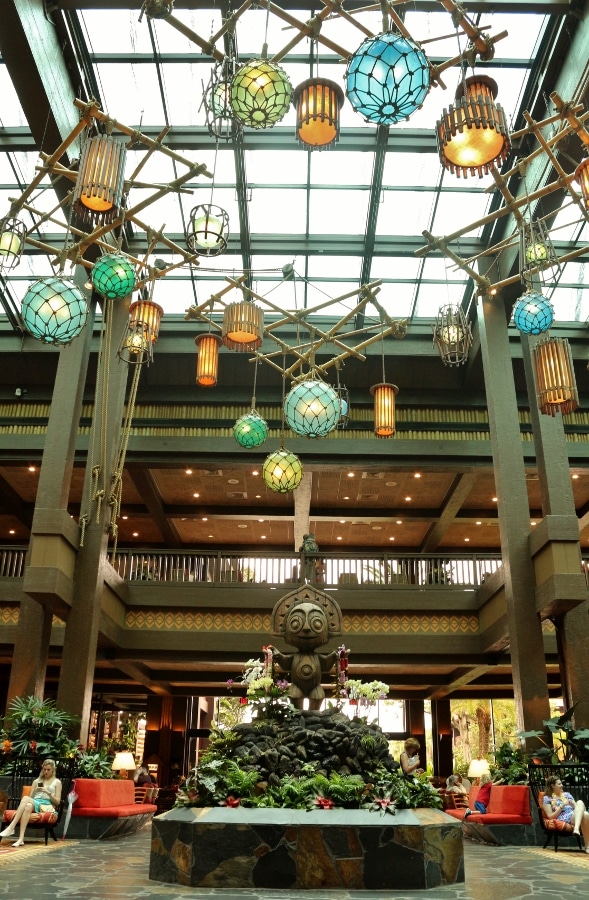 Disney\'s Polynesian Village Resort lobby with a tiki statue and colorful hanging lights