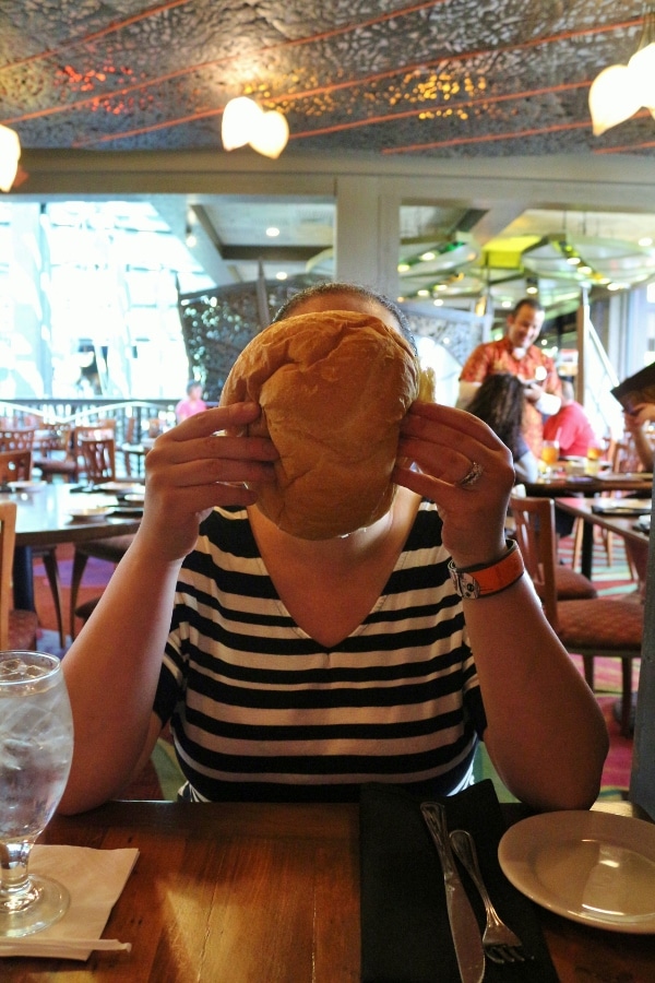 A woman holding a large round loaf of bread in front of her face