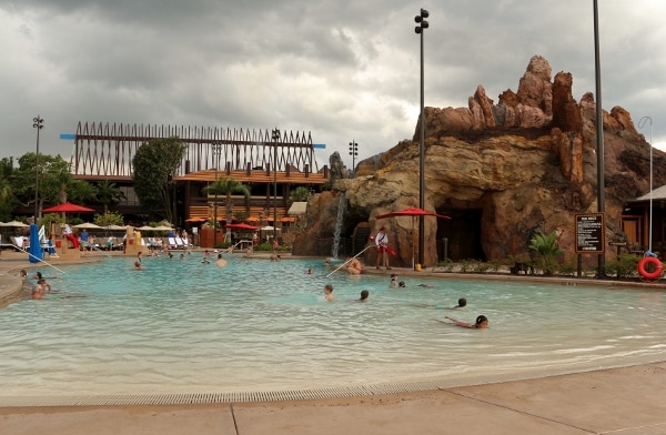 a group of people swimming in a pool with dark clouds looming overhead