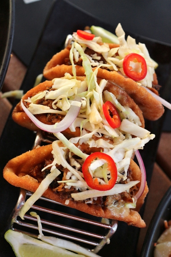 three tacos with cabbage served in a taco stand