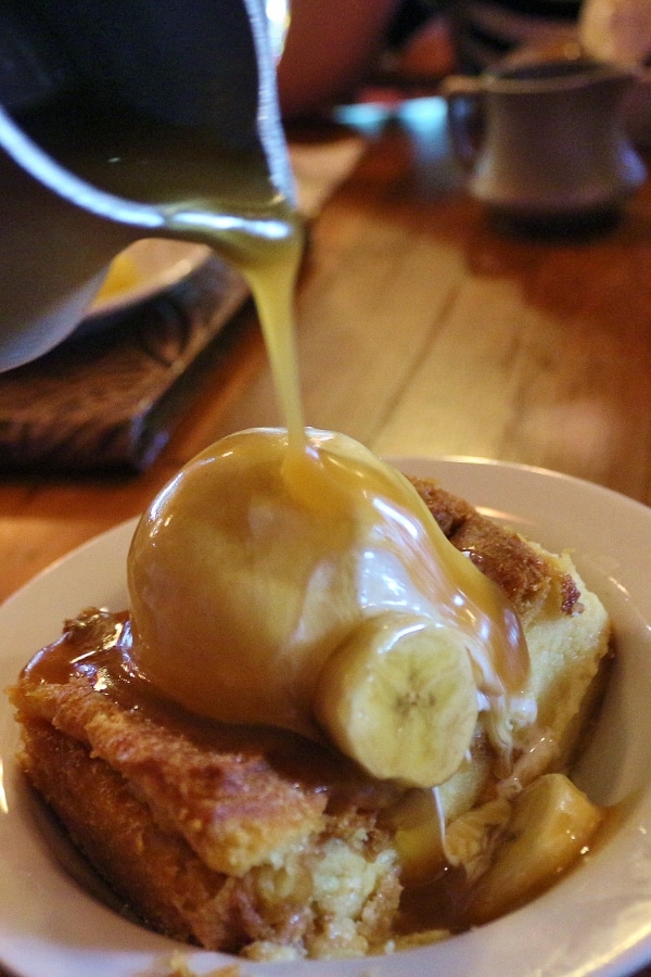 a plate of bread pudding with ice cream and banana sauce being poured over the top