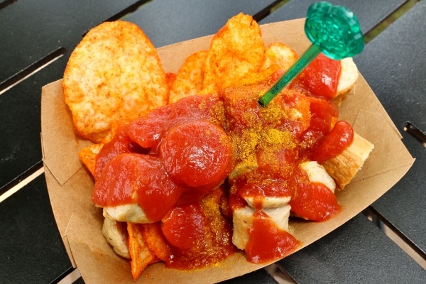 a plate of cut up sausage with a curried ketchup sauce and chips