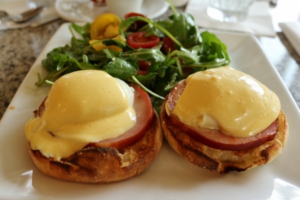 A close up of Eggs Benedict served with a side of salad