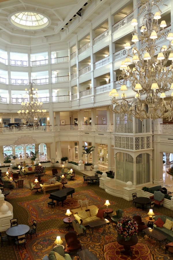 a vast hotel lobby with a piano, sitting areas, and tall ceilings with large chandeliers