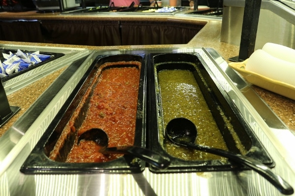 two large containers of red and green salsa in a buffet area